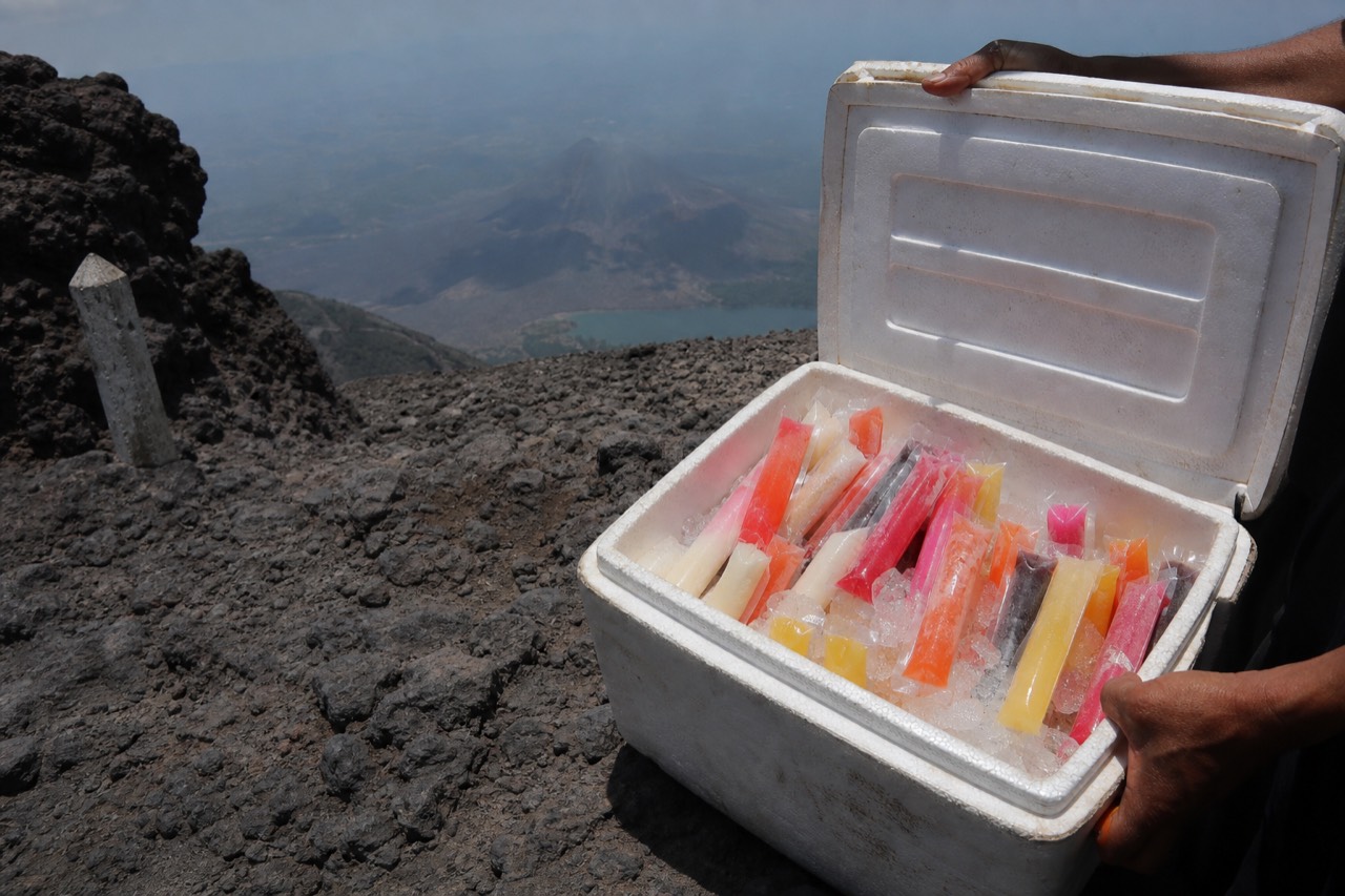 Vendor cooler with colorful paletas at the crater rim of Santa Ana Volcano with hikers resting behind