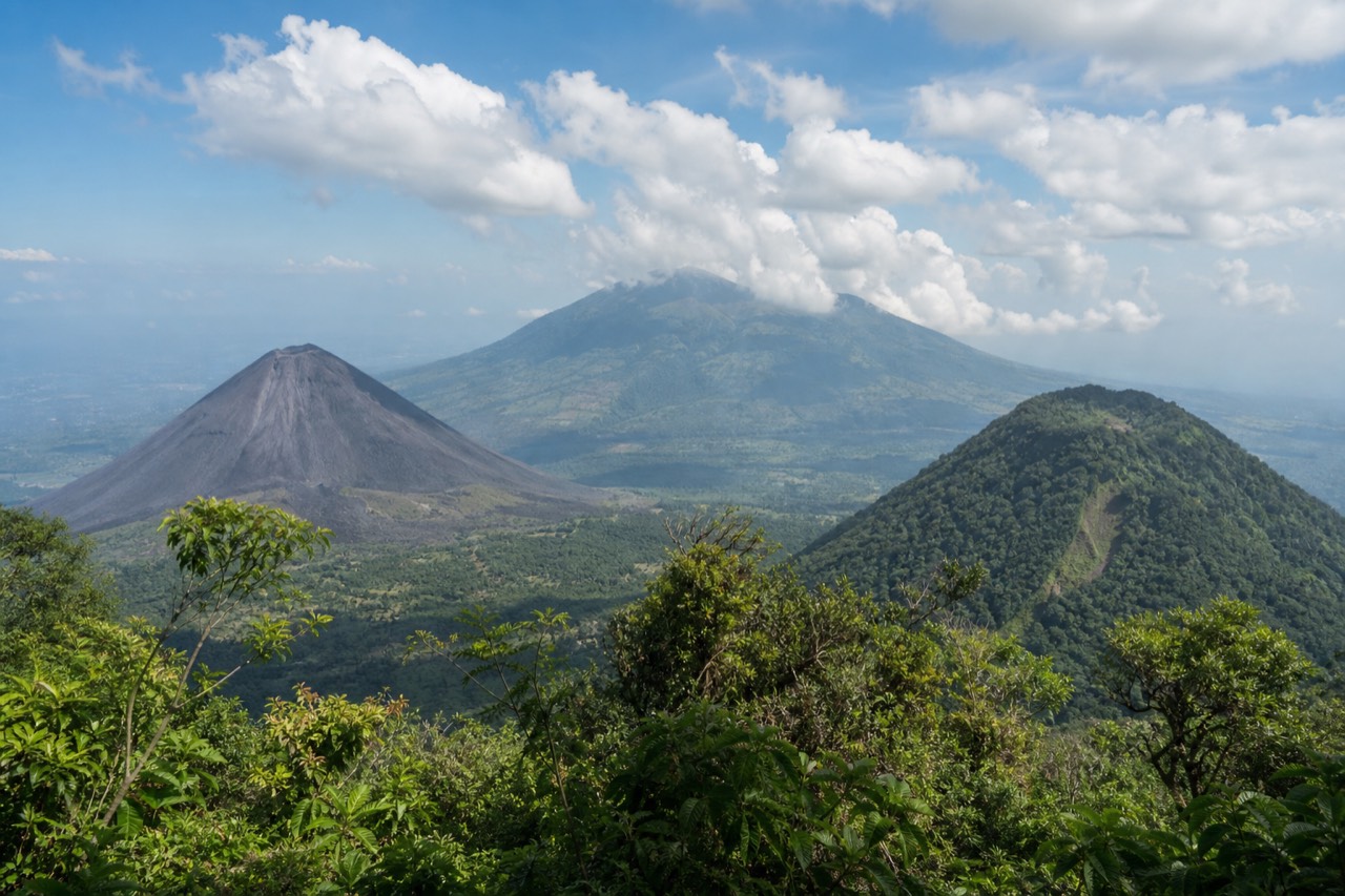 View from the Santa Ana Volcano trail across forested slopes to the black cone of Izalco